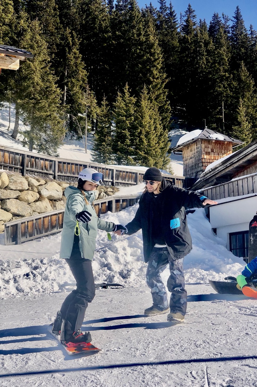a snowboard instructor is holding a snowboarder by the hand and showing her the way